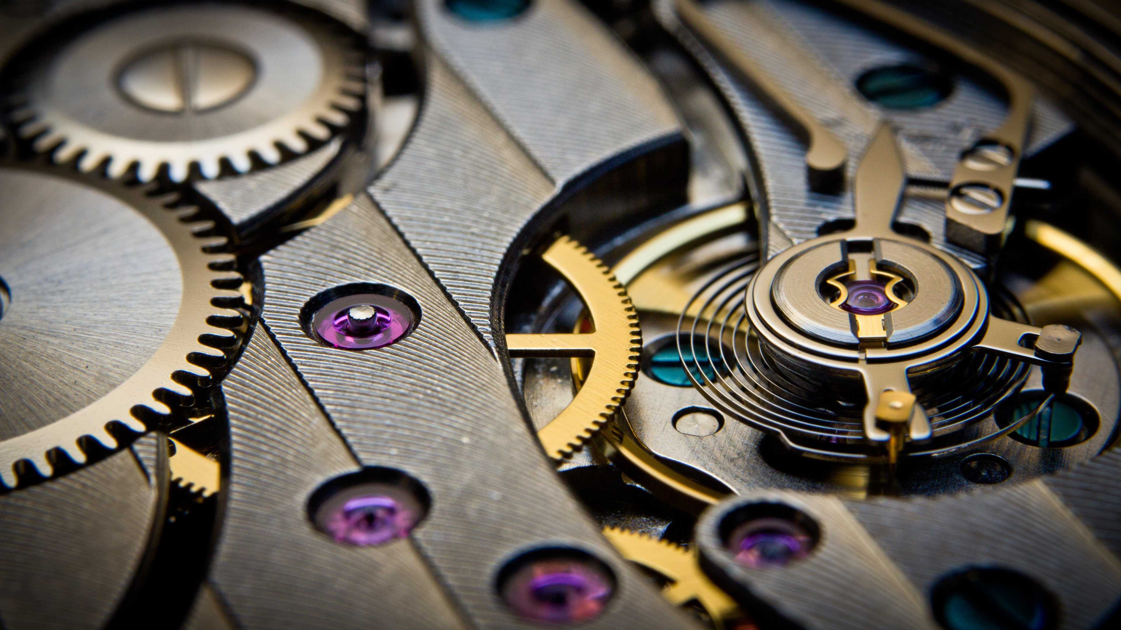 Extreme macro close-up of watch movement gears showing metallic gold and silver mechanical parts with purple-pink jewel accents
