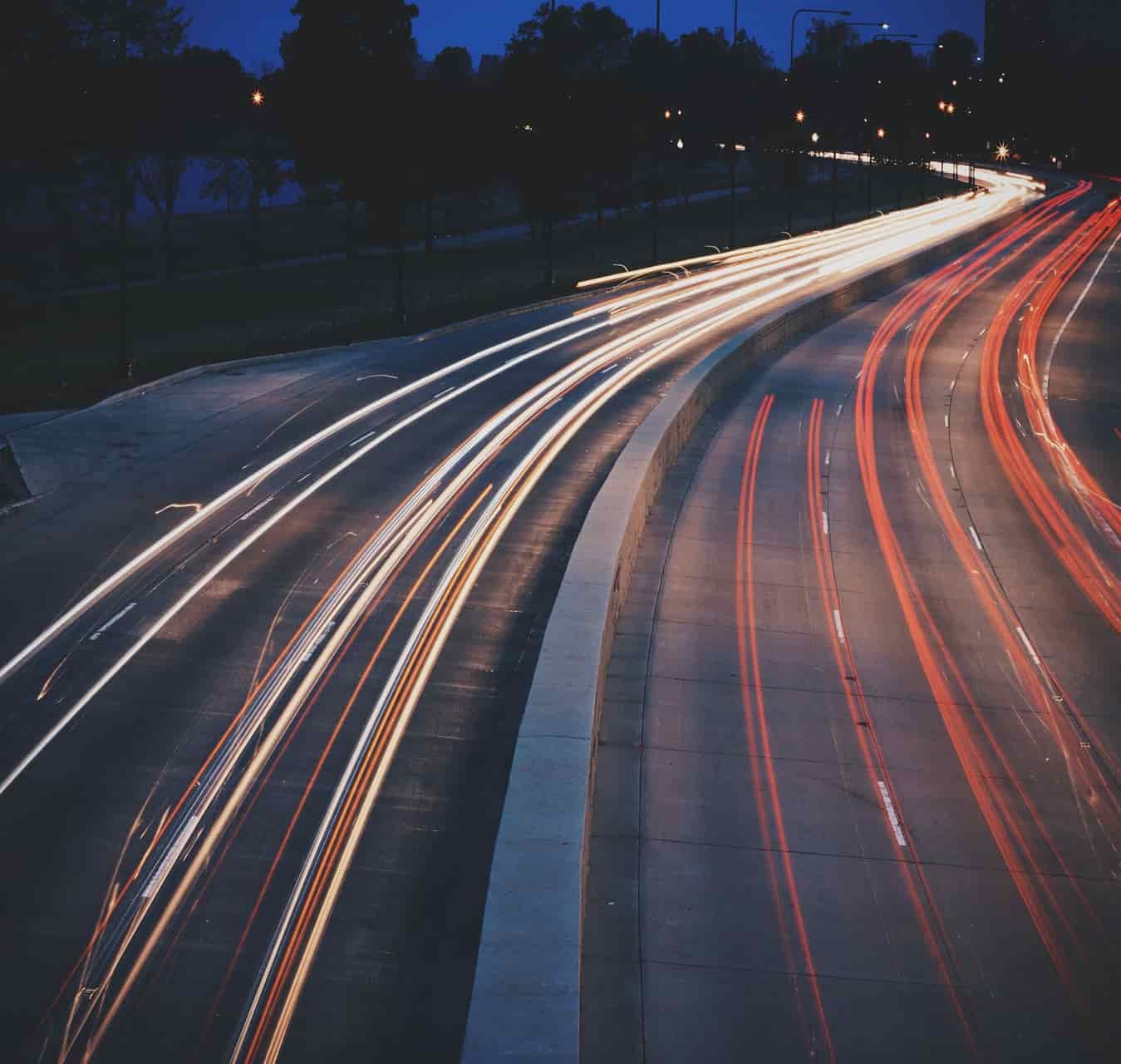 Long-exposure night view of a curved highway with sweeping streaks of white and red light trails against a dark navy sky, evoking motion and connectivity